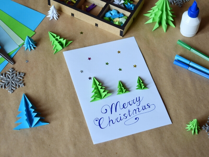 Zelené 3D stromčeky z papiera nalepené na vianočnej pohľadnici.