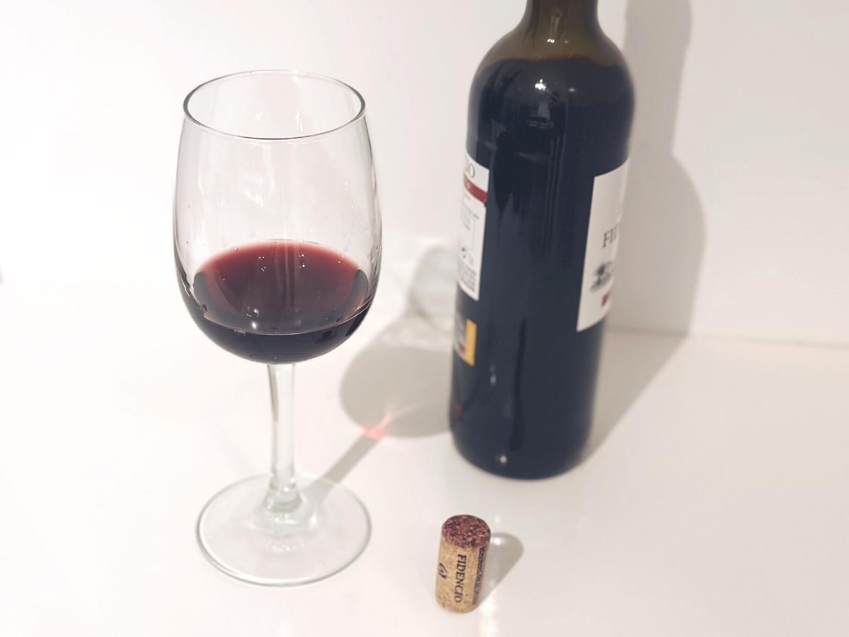 Pohár červeného vína pri otvorenej fľaši vína.