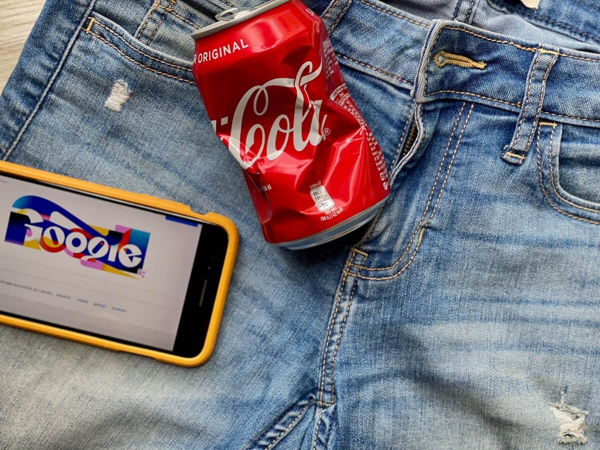 Plechovka Coca Coly a mobil s otvoreným vyhľadávačom Google položené na rifliach.