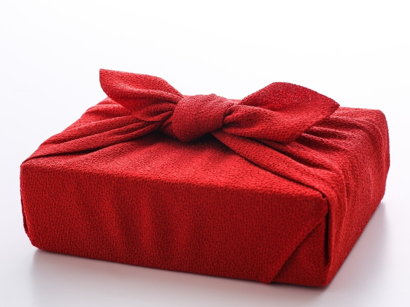Darček zabalený v červenej textílii japonským štýlom furoshiki.