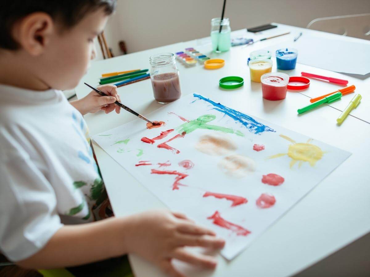 Malý chlapček maľuje obrázok so štetcom v ľavej ruke.