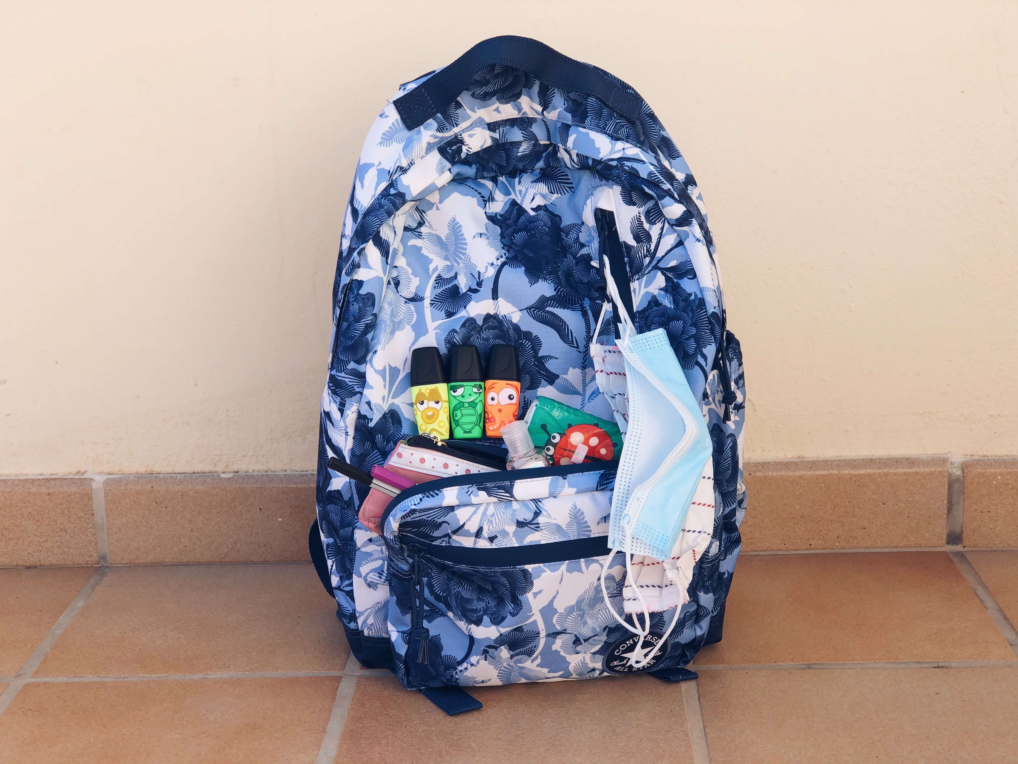 Textilné a jednorázové ochranné rúško zavesené na školskom batohu.